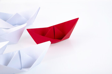 one red paper boat between many white paper boats. Copy space.