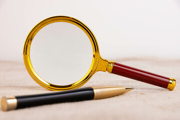 Magnifying glass of gold color, pen on a light background and linen fabric. A copy of the space.