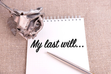 My last will, the text is written in a notebook lying on a linen linen and an iron rose flower.