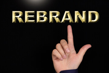 REBRAND text, a word written on a black background pointed to by a hand with the index finger of a person.