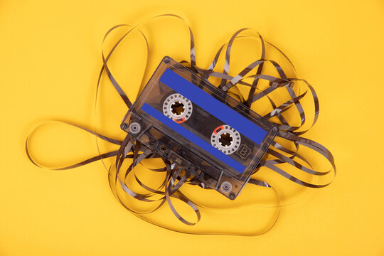 Old cassette tape with unwound tape on a yellow background.