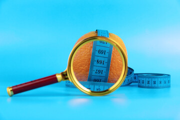 Diet concept with measuring tape, orange and magnifying glass for weight loss on blue background.