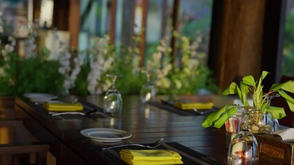 Dine in style at a tropical wooden dinner table adorned with a vibrant yellow napkin, adding a touch of elegance to your al fresco dining experience. Enjoy the warm ambiance. High quality 4k footage