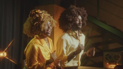 Groovy African-American couple in stylish outfits dancing together and having fun on retro party in a vintage studio. Medium shot, retro glow effect