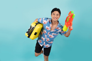 Handsome Asian tourist in summer clothes with water gun and luggage during Songkran festival on...