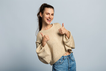 Cheerful attractive and positive girl showing thumb up gesture. Isolated, light grey background.