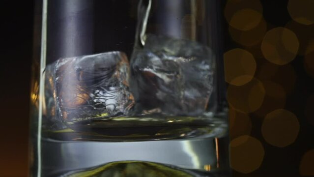 Whisky poured over ice cubes. Front on view. Dark and moody.