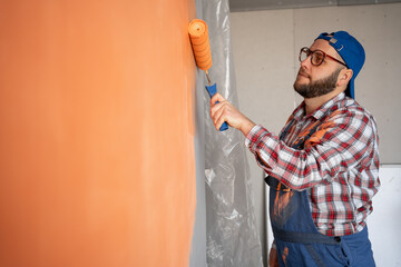 Handsome young painter man with happy smile painting the wall. Repair, building and home concept.