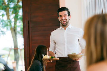 Waitress man serving food to group of diverse customer in restaurant, eatery client woman and man having smile and happy with service mind from cafes staff, lunch or dinner time lifestyle with family - 756266705