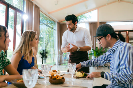Waitress man serving food to group of diverse customer in restaurant, eatery client woman and man having smile and happy with service mind from cafes staff, lunch or dinner time lifestyle with family