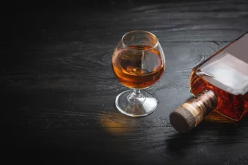 Gordijnen Glass of cognac and bottle on the dark background. © andranik123