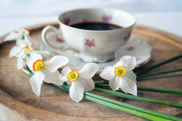 Still life with a delicate decoration of white daffodil flowers around a baroque fine porcelain coffee cup on a wooden tray - 756268729