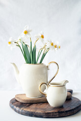 Still life with a blooming bouquet of white daffodils in an elegant porcelain teapot on a textured white background - 756268940