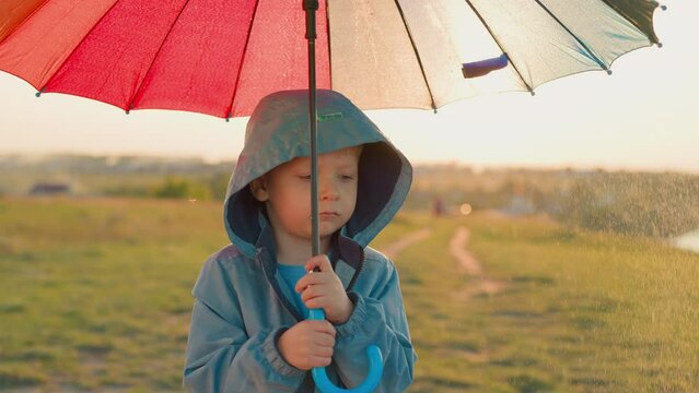Pensive kid with umbrella under rain in field