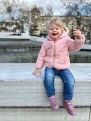 Enfant de 2 ans et demi vêtue d'une veste rose souriant devant une fontaine en Espagne à Séville