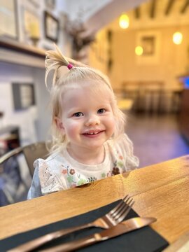 Jeune fille blonde de 2 ans et demi souriants coiffée d'une couette sur le haut de la tête à table