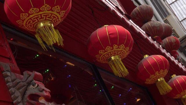From below of red traditional Chinese lanterns hanging and swaying on roof of building in city during daytime