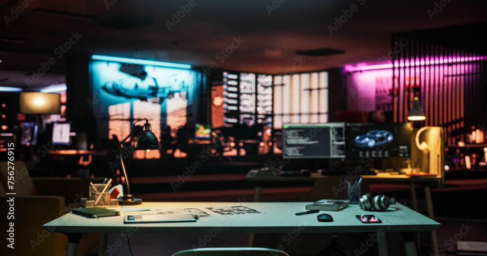 Poster Wide Shot of Desk with Smartphone, Laptop Computer and Notebook, Placed in an Empty Creative Office at Night. Modern Open Space Lit By Neon Lights for Game Development and Visual Media Production