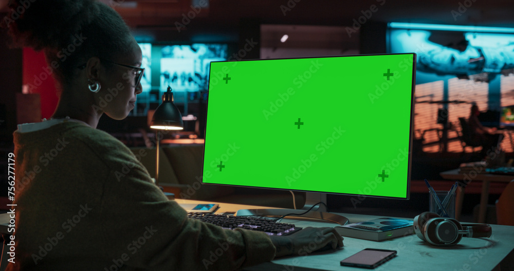 Poster portrait of creative black woman sitting at her desk using desktop computer with mock-up green scree