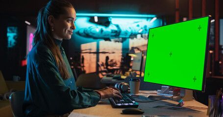 Fototapeta na wymiar Portrait of Young Woman Sitting at Her Desk Using Desktop Computer with Mock-up Green Screen. Female Caucasian Specialist Working on Computer with Chroma Key Display at Creative Agency