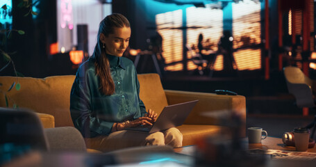 Portrait of White Creative Young Woman Working on a Laptop in Creative Office at Night. Female Team Lead Smiling While Checking her Team Performance Data, Sending Emails of Feedback