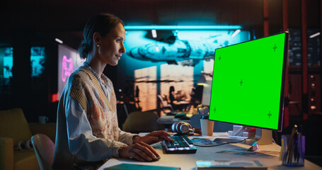 Portrait of Young Woman Sitting at Her Desk Using Desktop Computer with Mock-up Green Screen....