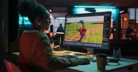 Portrait of Black Female Video Game Designer Creating Metaverse and Design Video Game Character in Creative Office at Night. Focused Woman Working on a New 3D Level on Her Desktop Computer