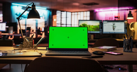Laptop Computer Standing on a Wooden Desk with a Green Screen Chromakey Mock Up Display. Creative Office Working Station for Game Developer and Graphic Designer in Creative Agency