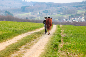 Rider walks her horse along a field path, landscape image in landscape format.