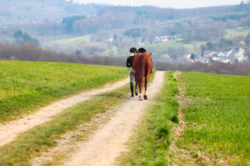 Rider walks her horse along a field path, landscape image in landscape format.