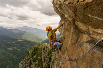 A man is climbing a rock wall with a yellow shirt and a backpack. He is wearing an orange helmet...