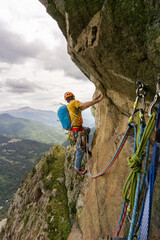 A man is climbing a rock wall with ropes attached to him. The man is wearing a yellow shirt and a...