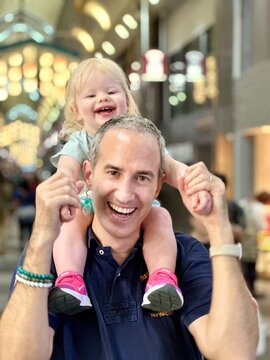 Enfant fille de 1 an et demi sur les épaules de son papa tous deux souriant