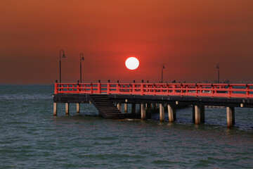 Red bridge that extends into the sea and view of the sunset in the evening time.