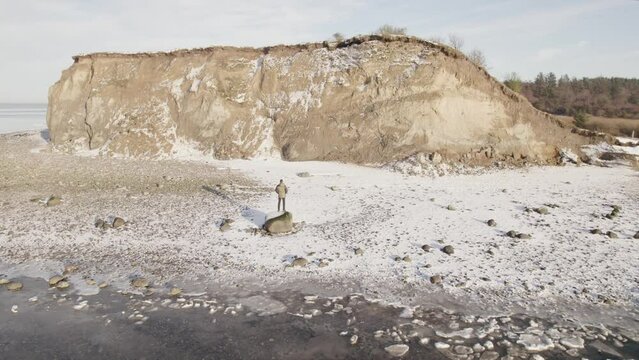 Aerial Fly Away Shot Of A Lonely Man Standing By A Cliff Near The Ocean With Sky Reflection