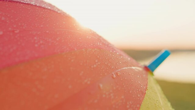 Raindrops fall on bright umbrella surface. Colorful parasol adds cheerful touch to scene with vibrant hues contrasting beautifully with soft gray of spring sky