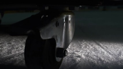 Rotating wheel of cart on dark hockey rink at flashlight closeup. Skating rink service equipment driving along. Sports stadium cleaning
