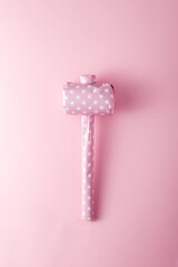 Vintage hammer packaged in pink polka dot gift paper on a pink background, top view.