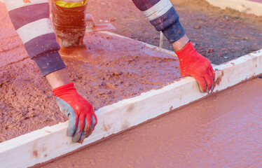 Builders pouring and levelling wet ready-mix concrete into formwork   during new footpath...