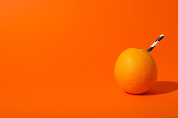 Orange with cocktail straw on orange background, space for text
