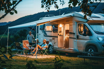 A couple sits comfortably outside their motorhome, enjoying a beautiful sunset together in the countryside