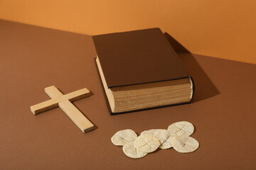 Wooden cross, book and liturgical bread on brown background
