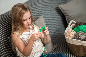 Little girl to knit while sitting on couch enjoying her hobby - obrazy, fototapety, plakaty