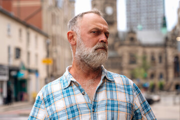 portrait of a bearded mature man looking suspiciously at the camera, walking in the city 