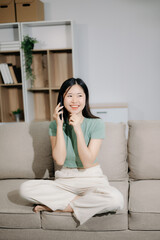 Young asian woman using smartphone and tablet while seated on couch at home.