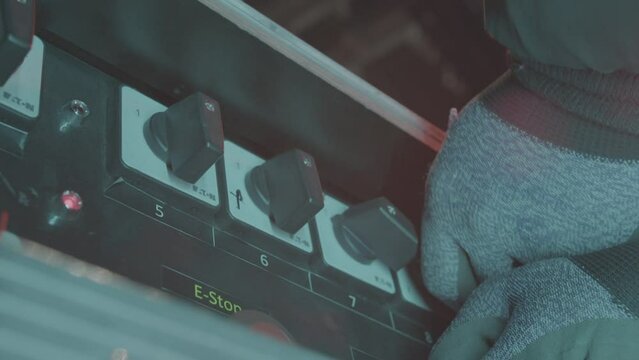 Worker hand in glove turns emergency stop levers on control panel closeup. Employee operates with machine tool at manufacturing plant
