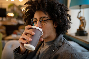 Young curly-haired man sitting in a hotel hall and drinking coffee