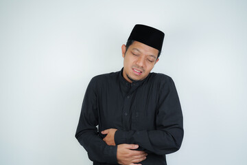 Obraz na płótnie Canvas Asian Muslim man having stomach ache, bending over and holding hands on stomach, uncomfortable due to stomach cramps, gastric pain