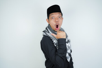 Wow face shocked expression Asian Muslim man wearing Arab turban sorban pointing hand finger at empty space on isolated background