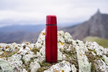 Red steel thermos, metal thermo bottle in the mountains